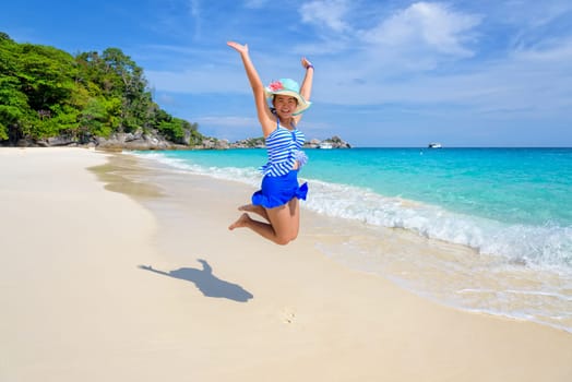 Tourist girl in a blue white striped swimsuit jumping with happy on the beautiful beach and sea during summer at Koh Miang Island, Mu Ko Similan National Park, Phang Nga province, Thailand
