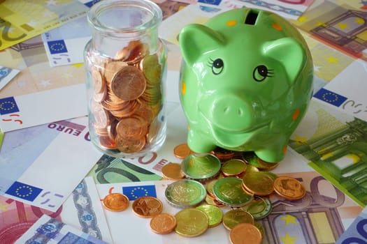 Piggy bank and glass with euro coins on banknotes