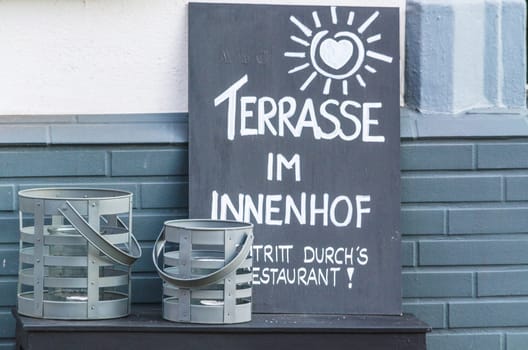 Labeled wooden billboard on the sidewalk at a restaurant.