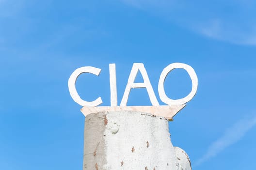 Lettering Ciao on an old tree trunk in front of blue sky.