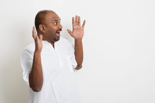 Portrait of mature casual business Indian man shout and get shocked, standing on plain background with shadow.