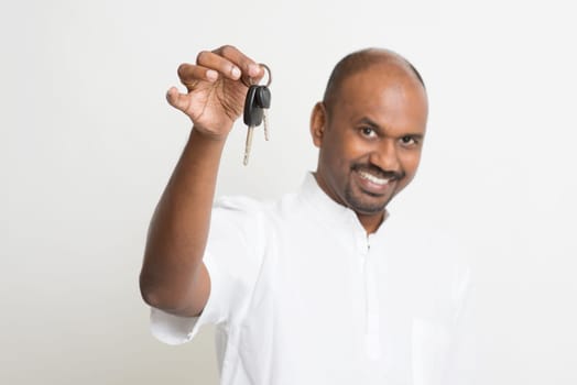 Mature Asian Indian estate agent or salesman showing a key, India male business man, standing on plain background with shadow.