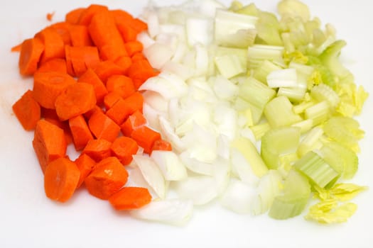 Orange carrots, white onions and green and yellow celery vegetables sliced into pieces to add them to lentil soup.