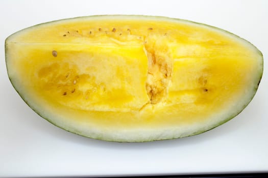 One quarter of a yellow watermelon fruit cut lengthwise resting on a white plastic cutting board on a black granite countertop.