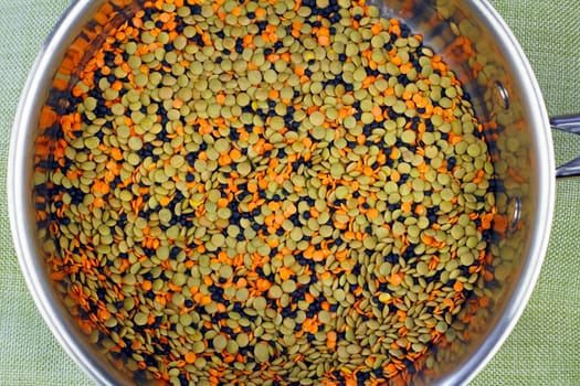 Organic orange, black and green dry, uncooked lentils mixed together in a round stainless steel pan ready to cook and add to a recipe. Tricolor lentils in a saucepan.