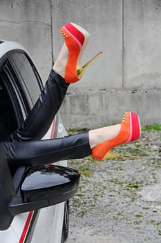 A woman stretches her legs out of the window of a car with stick shoes