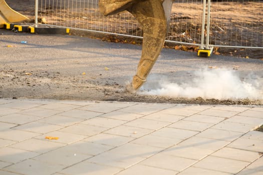 Excavator Ripping Asphalt with fence behind it.