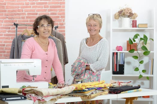 Two cheerful seamstresses working together in their fashion workshop