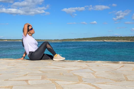 Latina woman, 48 years old, sitting on a pier in Colonia de Sant Jordi, Mallorca, Spain. A sunny early spring day by the turquoise sea, enjoying the peaceful coastal view.