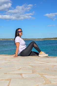 Latina woman, 48 years old, sitting on a pier in Colonia de Sant Jordi, Mallorca, Spain. A sunny early spring day by the turquoise sea, enjoying the peaceful coastal view.