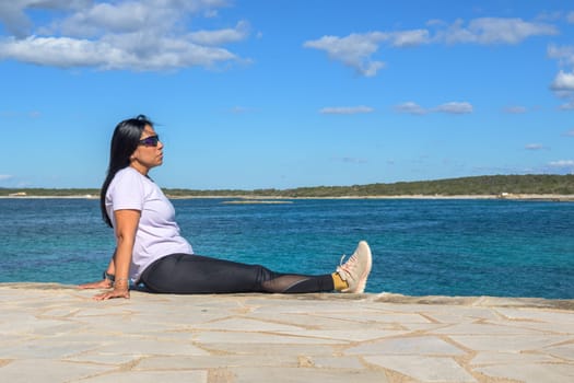 Woman sitting by the ocean, wearing sunglasses, beautiful latina woman by the sea in Colonia San Jordi, Balearic Islands, Majorca, Spain,