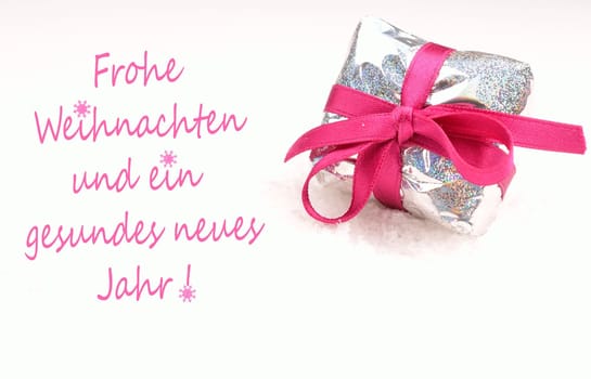 Christmas present in silver with a pink bow on a white snow background, German Merry Christmas background