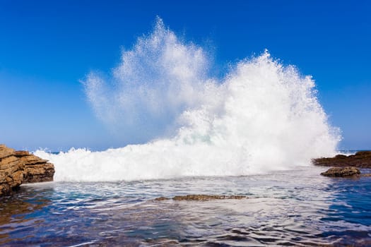 Ocean wave crashing exploding along rocky shoreline exploding white water power