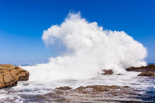 Ocean wave crashing exploding along rocky shoreline exploding white water power