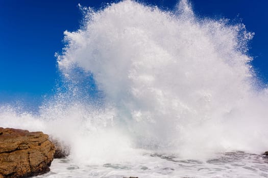 Ocean wave crashing exploding along rocky shoreline exploding white water power
