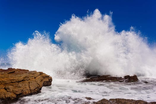 Ocean wave crashing exploding along rocky shoreline exploding white water power