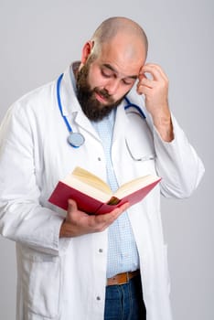 young bearded doctor in white coat is reading a book