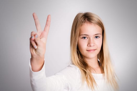 nice blond girl in front of gray background showing victory sign