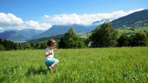 little girl playing in a meadow in the mountains