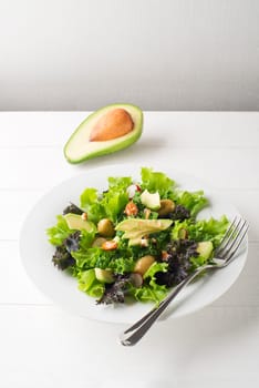 Fresh mixed green salad with avocado on white plate