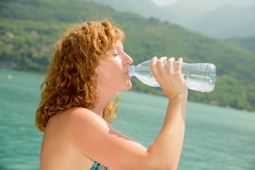young woman drinks water with a bottle on the beach