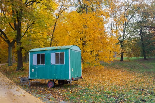 Green-blue construction car in the park in front of autumnally discoloured forest