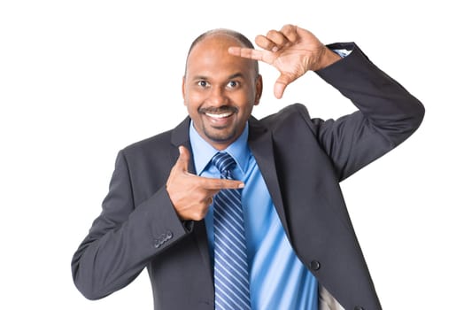Cheerful Indian businessman making fingers frame and peeping through, on plain background