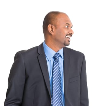Portrait of mature Indian businessman smiling and looking to side, standing on plain background.