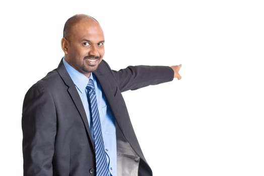 Indian businessman pointing away to copy space, on plain background.
