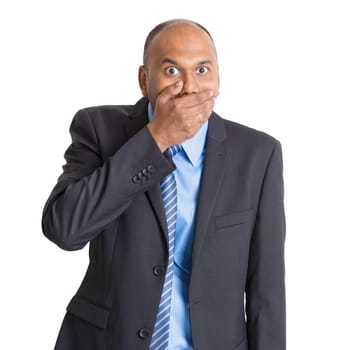 Portrait of shocked mature Indian businessman covered mouth, standing on plain background with shadow.