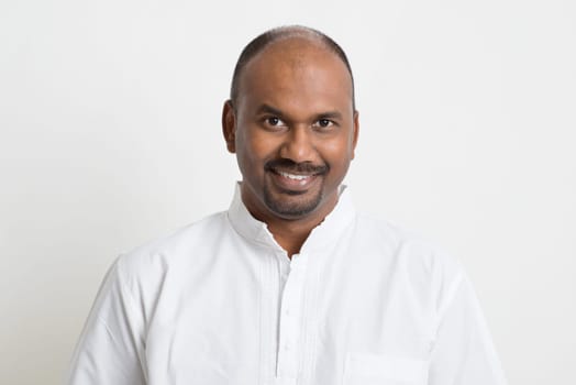 Portrait of mature casual business Indian man smiling, standing on plain background with shadow.