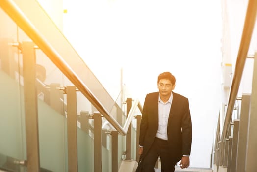 Asian Indian corporate businessman in suit with briefcase ascending steps.