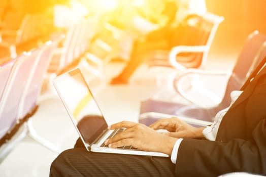 Business man using laptop while waiting his flight at airport, beautiful golden sunlight background.