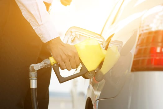 Close up business man pumping gasoline fuel in car at gas station, golden sunlight background.