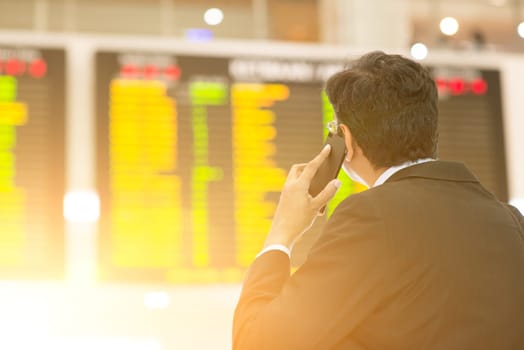 Asian Businessman looking at airport flight timetable and on the phone, filter sun.