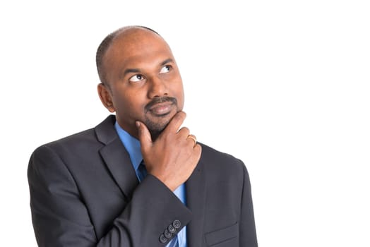 Portrait of mature Indian businessman looking up and thinking, copy space on side, standing on plain background with shadow.