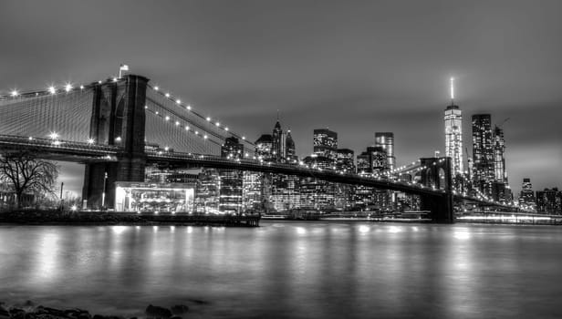 Brooklyn bridge and New York City Manhattan downtown skyline at dusk with skyscrapers illuminated over East River panorama. Copy space. Black and white image.