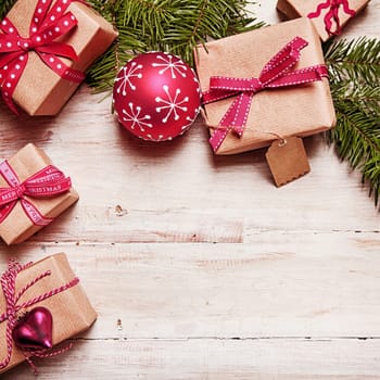Christmas border with decorative gifts tied with bows, baubles and pine foliage on a rustic wood background with copyspace in square format