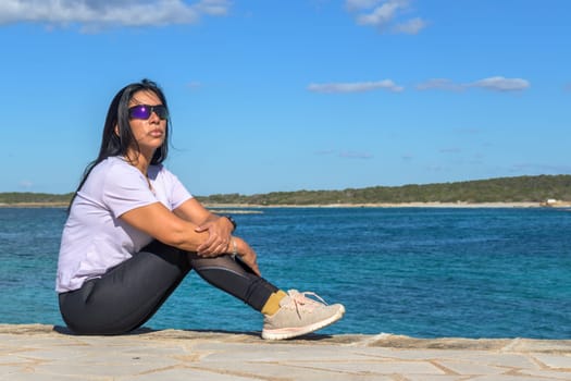 Woman sitting by the ocean, looking into the distance, beautiful latina woman by the sea in Colonia San Jordi, Balearic Islands, Majorca, Spain