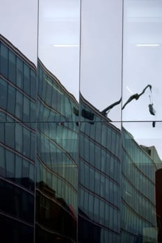 The mirroring of a high-rise facade to which a crane with a cabin for window cleaners is attached.