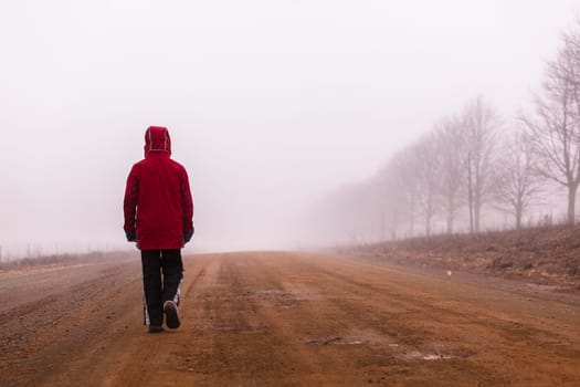 Teenager boy walking mountain rural farm dirt road in morning cloud mist