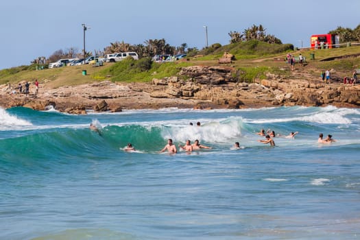 Ocean waves swimmers men women boys girls  in beach rocky landscape
