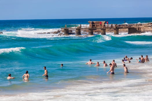 Ocean waves swimmers men women boys girls  in beach rocky landscape