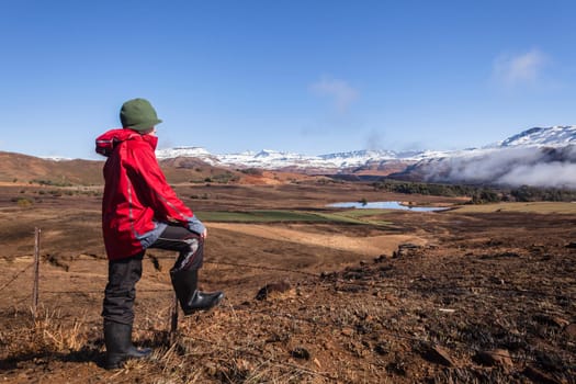 Teen boy overlooks mountain snow valley  green black contrasted scenic landscape