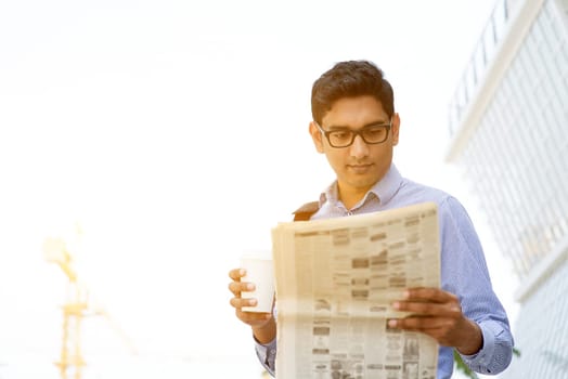 Asian Indian business people holding coffee cup and reading newspaper on the way to work place in morning. Handsome male model.