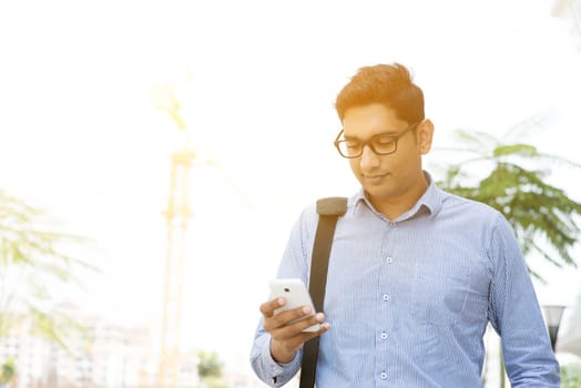 Asian Indian business people texting using smartphone while walking to office, modern urban sunrise view.
