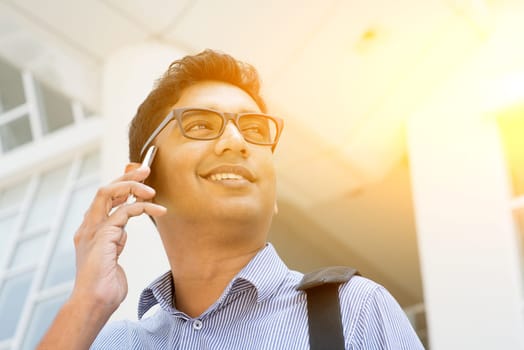 Indian businessman talking on phone in front modern office building. Urban view with sunlight.
