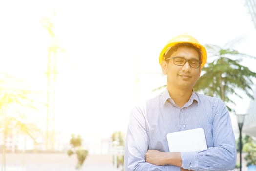 Portrait of a Asian Indian male contractor engineer with hard hat holding tablet pc at construction site.
