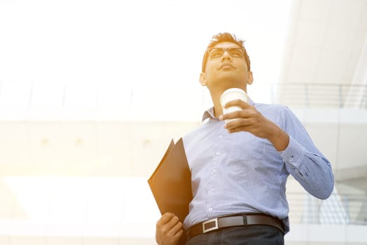 Asian Indian business man hand holding take away hot coffee cup and file folder in morning sunlight, outdoors modern office business concept.