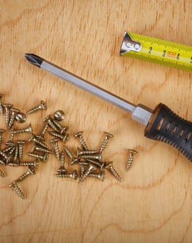Screws and screwdriver on wooden background.